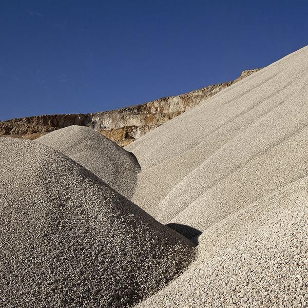 Grandes montones de grava de color claro contra un acantilado color canela y un cielo azul claro.