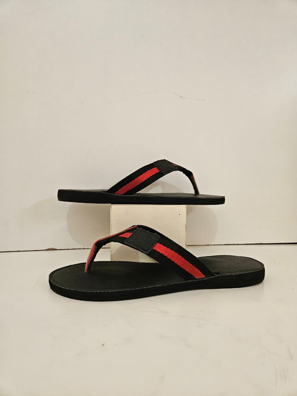 A pair of black and red flip flops are sitting on top of a white block.