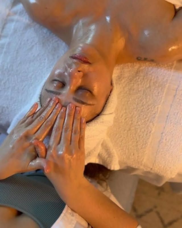 Mujer recibiendo masaje facial en un spa; manos en la cara; ojos cerrados, acostada sobre una toalla.