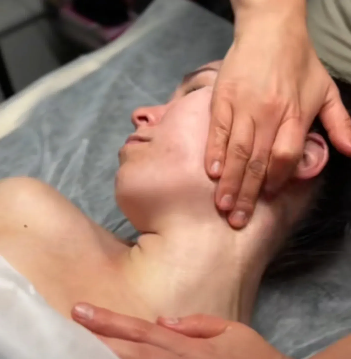 Persona recibiendo un masaje facial. Una mano masajea la mandíbula y el cuello en un ambiente de spa.