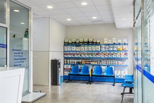 Una sala de espera en una farmacia con sillas azules y un mostrador.