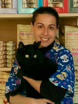 Una mujer sostiene un gato negro frente a un estante que dice natural.