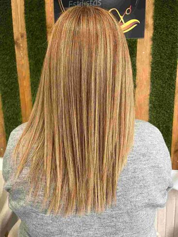 Vista trasera de una persona con cabello largo con mechas, vestida con una camisa gris, sobre un fondo verde.