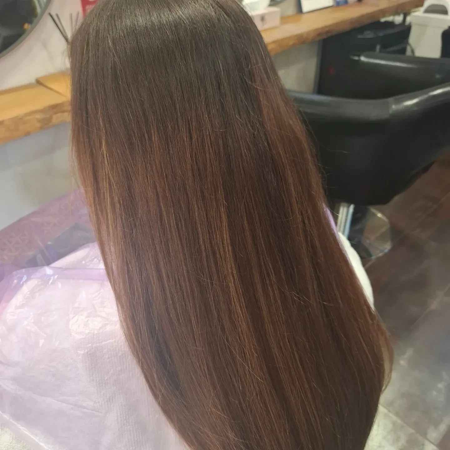 Cabello largo, liso y castaño visto desde atrás en una silla de peluquería.