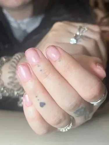 Mano con uñas rosa pálido y anillos plateados cerca de la cámara