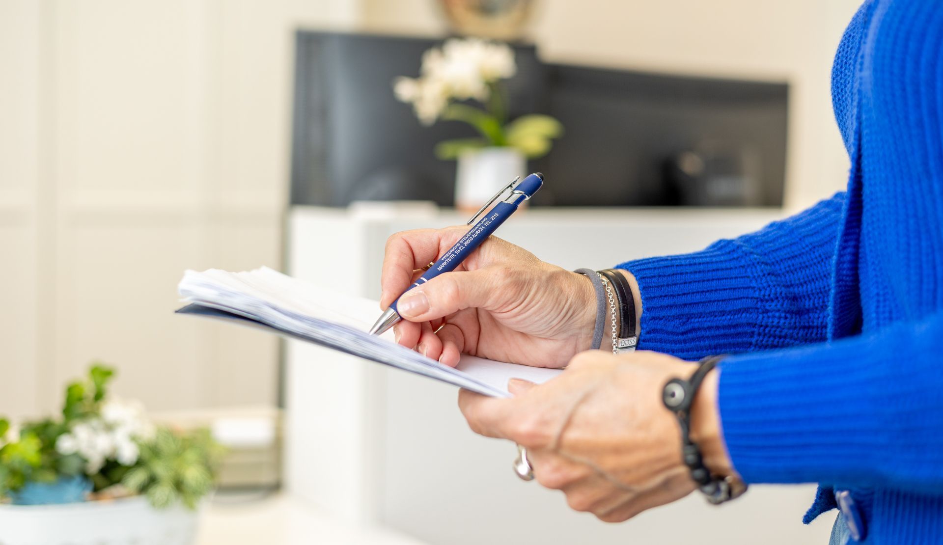 Eine Frau in einem blauen Pullover schreibt mit einem Stift in ein Notizbuch.