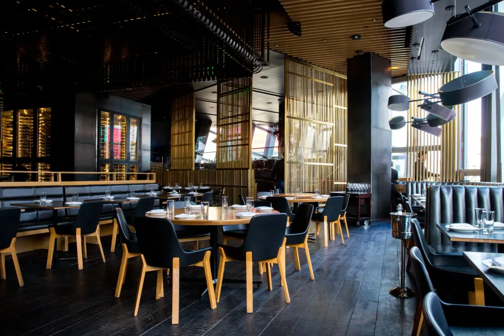 Intérieur de restaurant moderne avec tables noires, chaises en bois et éclairage suspendu chaleureux