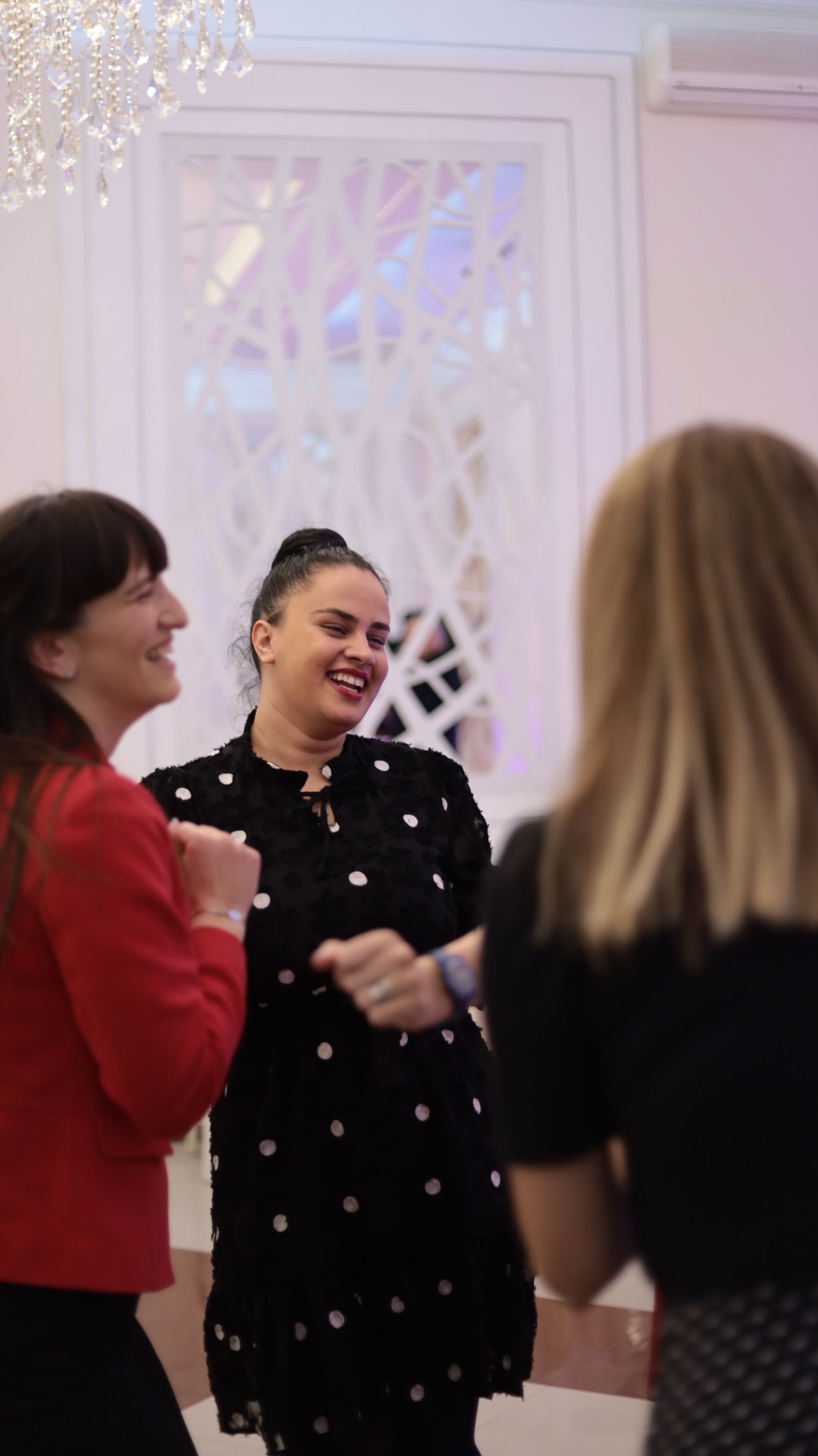 Trois personnes discutent lors d'une réunion amicale, souriant dans une pièce lumineuse à la décoration blanche.