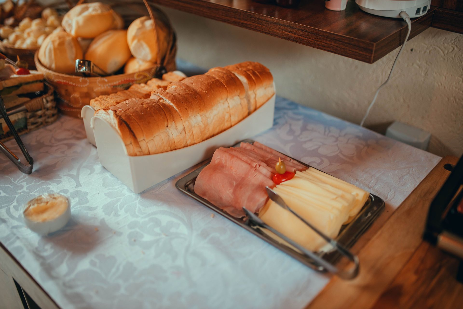 Table de petit-déjeuner avec pain tranché, jambon, fromage et petits pains sur une nappe blanche