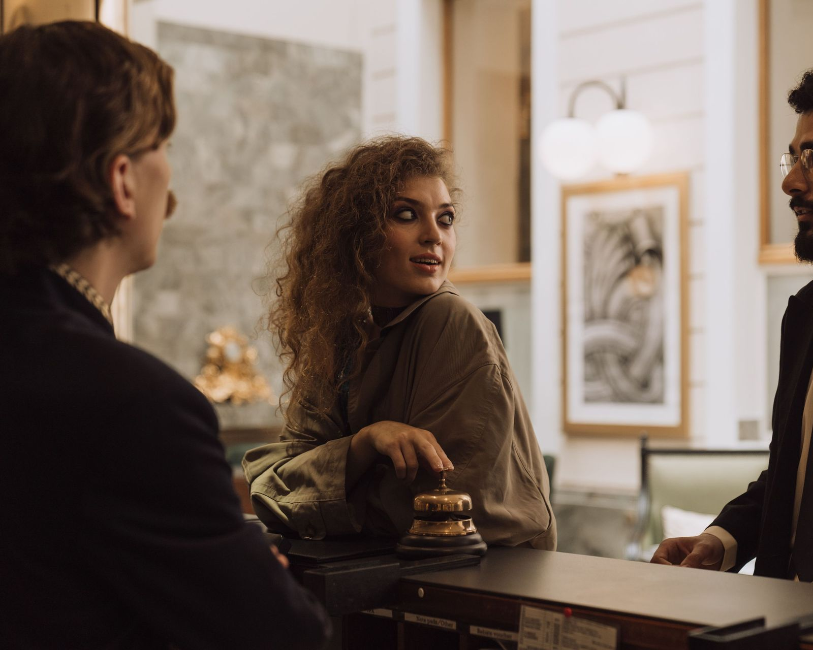 Trois personnes discutent à la table d'un café ; une femme sourit et se tourne vers quelqu'un sur sa droite.
