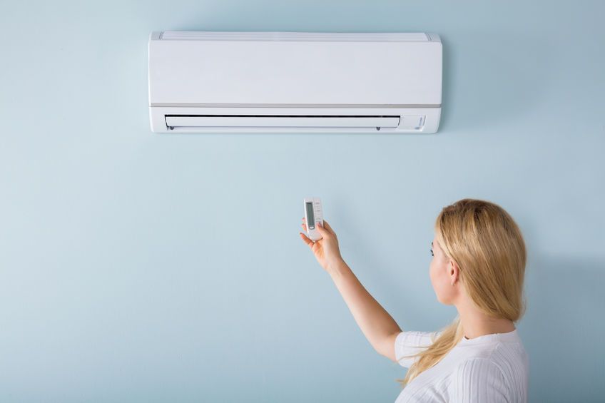 Una mujer está ajustando la temperatura de su aire acondicionado con un control remoto.