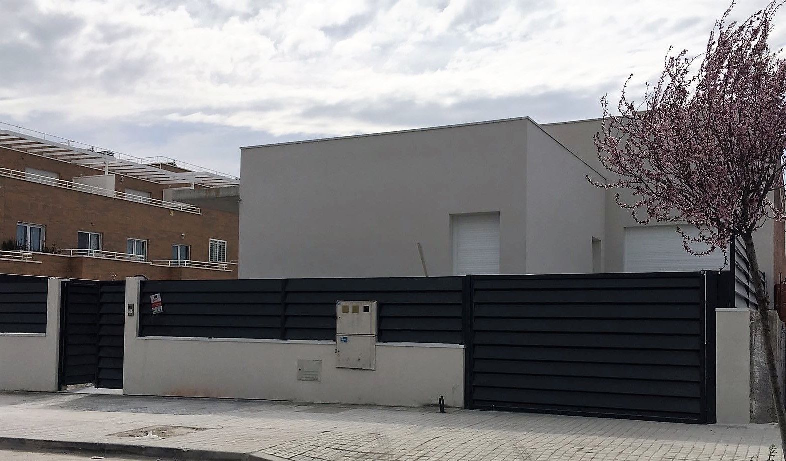 Una casa con una valla negra y un árbol delante de ella.