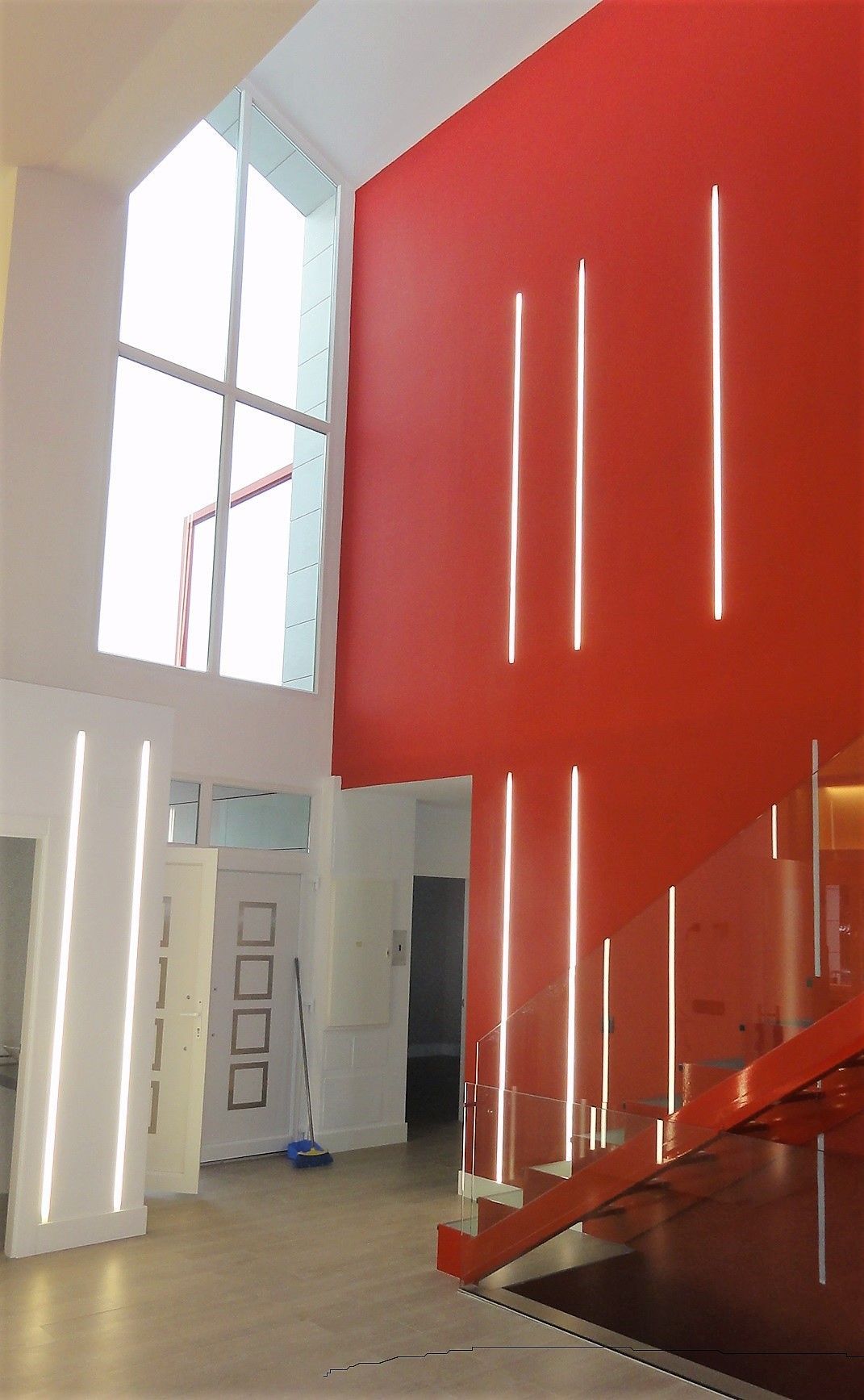 Una escalera con una pared roja y una barandilla de cristal.