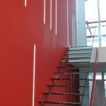 Una escalera con una pared roja detrás y una barandilla de cristal.