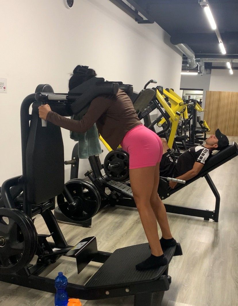 Une femme est accroupie sur une machine dans une salle de sport tandis qu'un homme est allongé sur un banc.