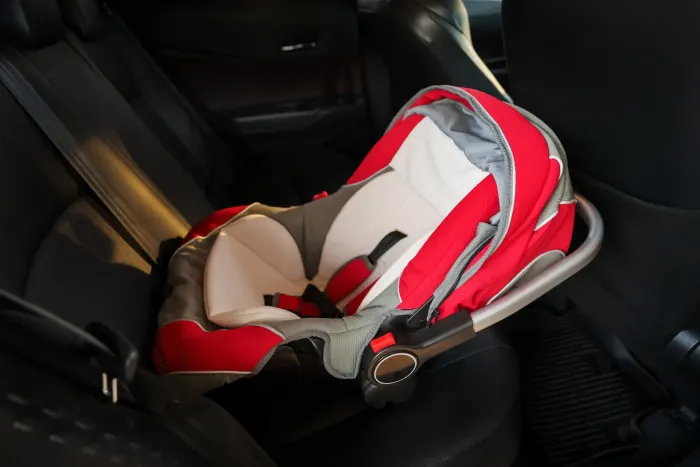Asiento infantil para automóvil de color rojo y blanco, fijado en el asiento trasero de un automóvil.