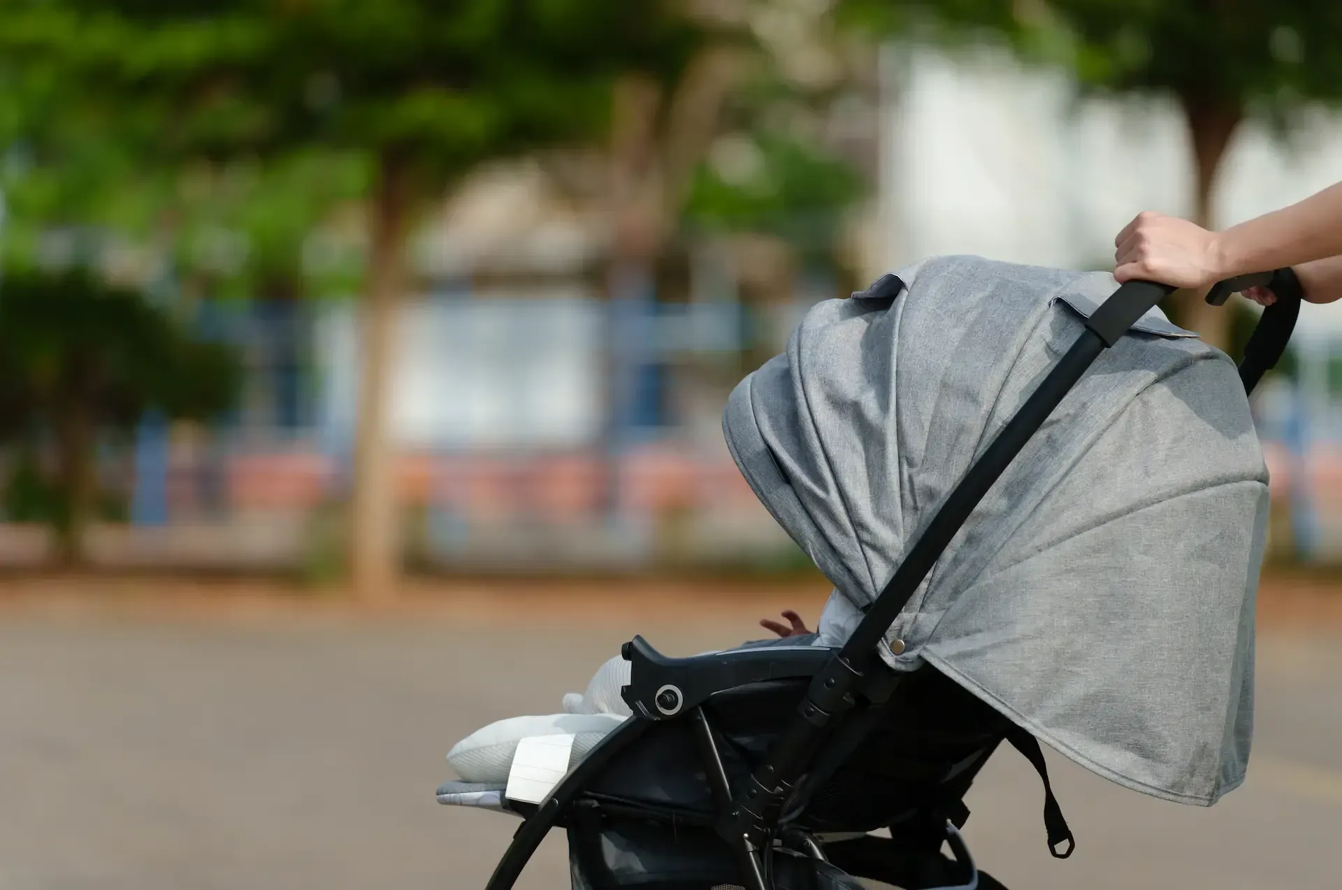 Persona empujando un cochecito gris por una carretera con un fondo borroso.
