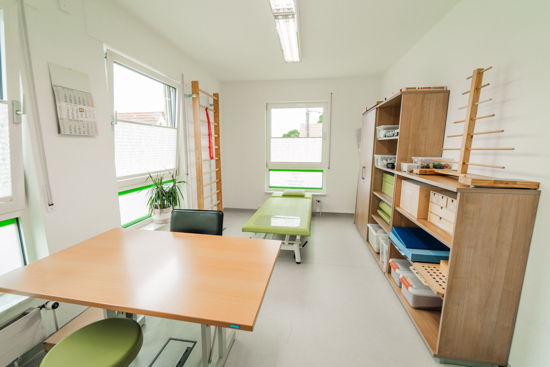 Zimmer mit zwei Fenstern und Holzmöbeln und einer grünen Liege