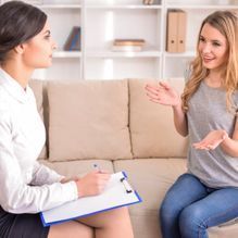 Una mujer está sentada en un sofá hablando con un psicólogo.