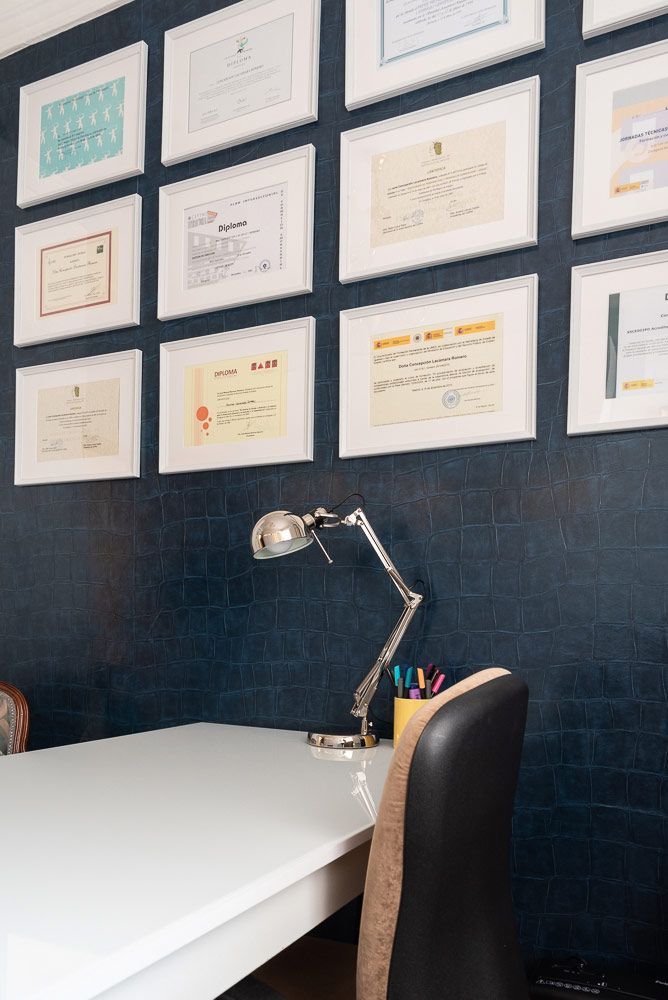 Un escritorio con una lámpara y una silla frente a una pared con certificados.