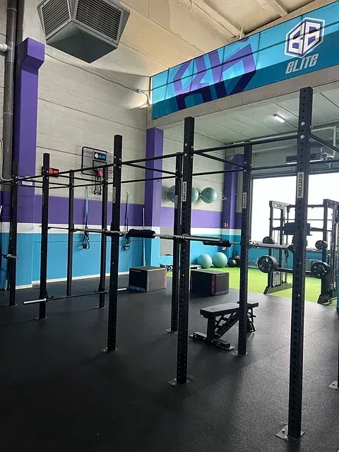 Interior de gimnasio con equipos de entrenamiento negros, paredes azules y violetas y un logotipo colorido.