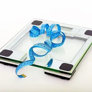 Una báscula de baño con una cinta métrica azul sobre ella, lo que sugiere pérdida de peso o medición del cuerpo.