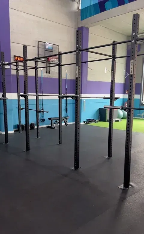 Interior de gimnasio con plataforma de dominadas negra, paredes moradas y azules y varios equipos de fitness.