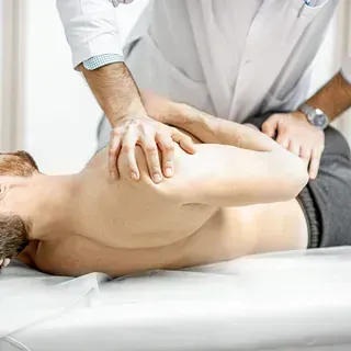 Quiropráctico ajustando la espalda de un paciente; el hombre está sin camisa en una mesa, el médico lleva una bata blanca.