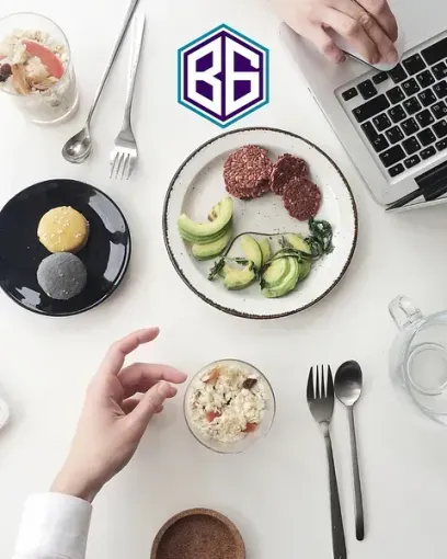 Vista aérea de una mesa blanca con un plato de comida, una computadora portátil y manos interactuando con la comida y los cubiertos. El logotipo
