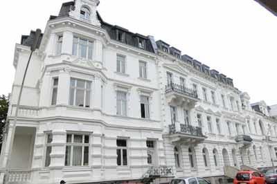 Ein großes weißes Gebäude mit vielen Fenstern und davor geparkten Autos.