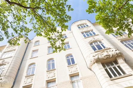 Blick nach oben auf ein hohes Gebäude mit vielen Fenstern, umgeben von Bäumen.