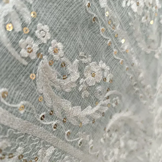 Un primer plano de una tela de encaje blanco con flores y lentejuelas.