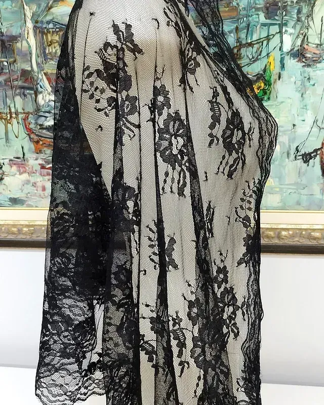 Un pañuelo de encaje negro está sobre un maniquí delante de un cuadro.