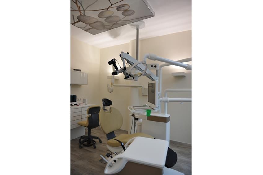 Eine Zahnarztpraxis mit einem Zahnarztstuhl und einem Mikroskop, das von der Decke hängt.