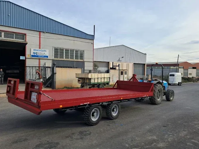 Remolque de plataforma plana roja enganchado a un camión en un patio industrial