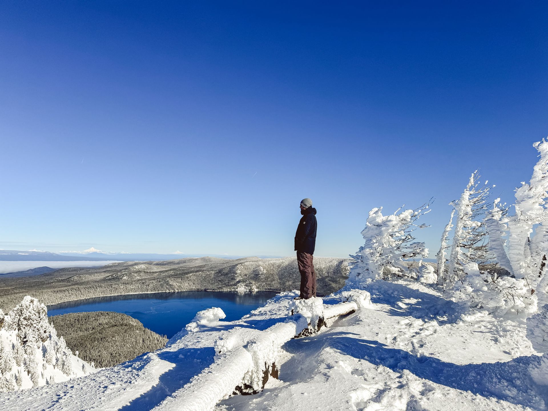 Man standing on a snowy trail overlooking Paulina Lake in Newberry National Monument in Central Oregon