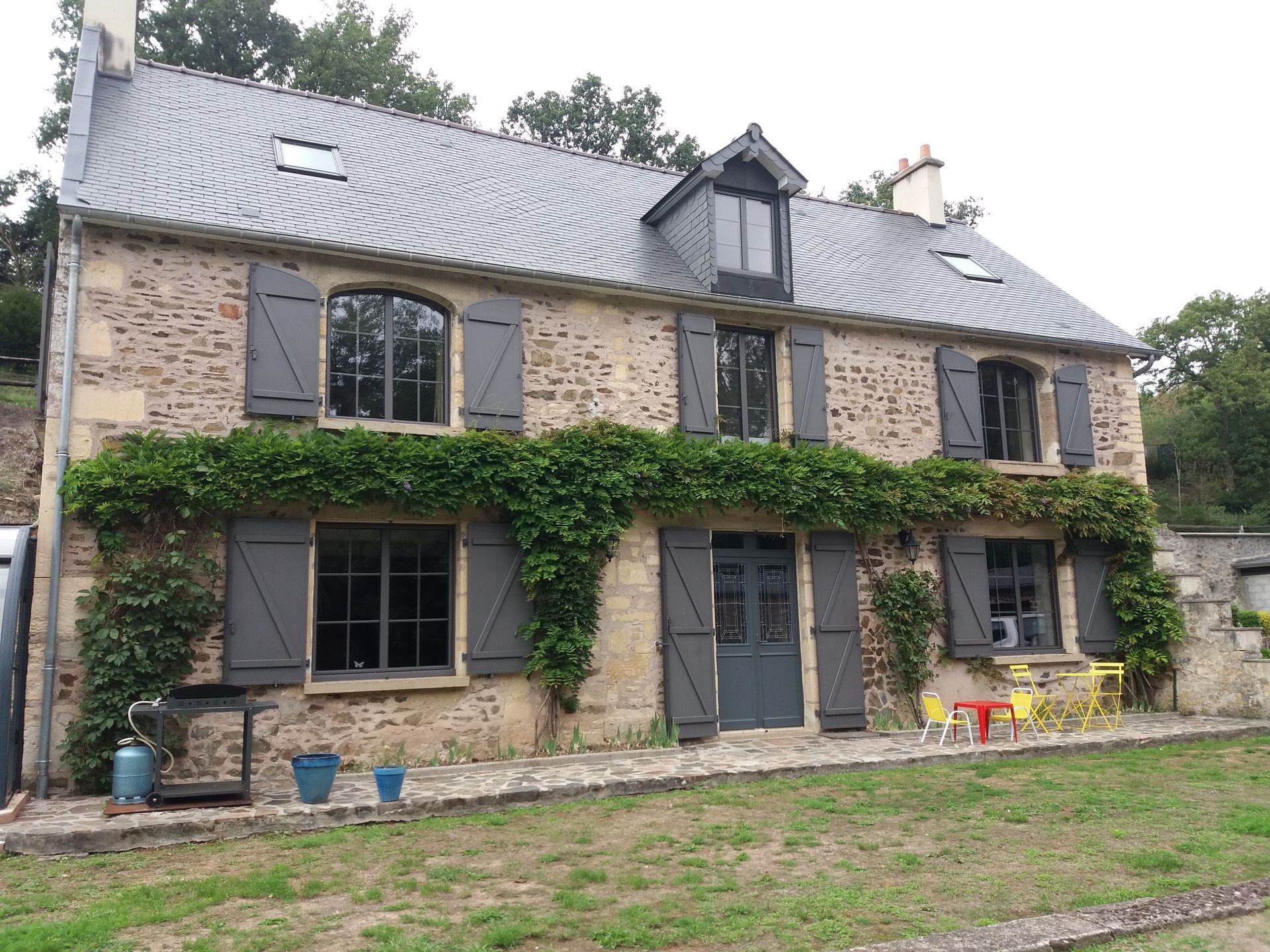 Façade d'une maison en pierre avec de nombreuses fenêtres et des volets.