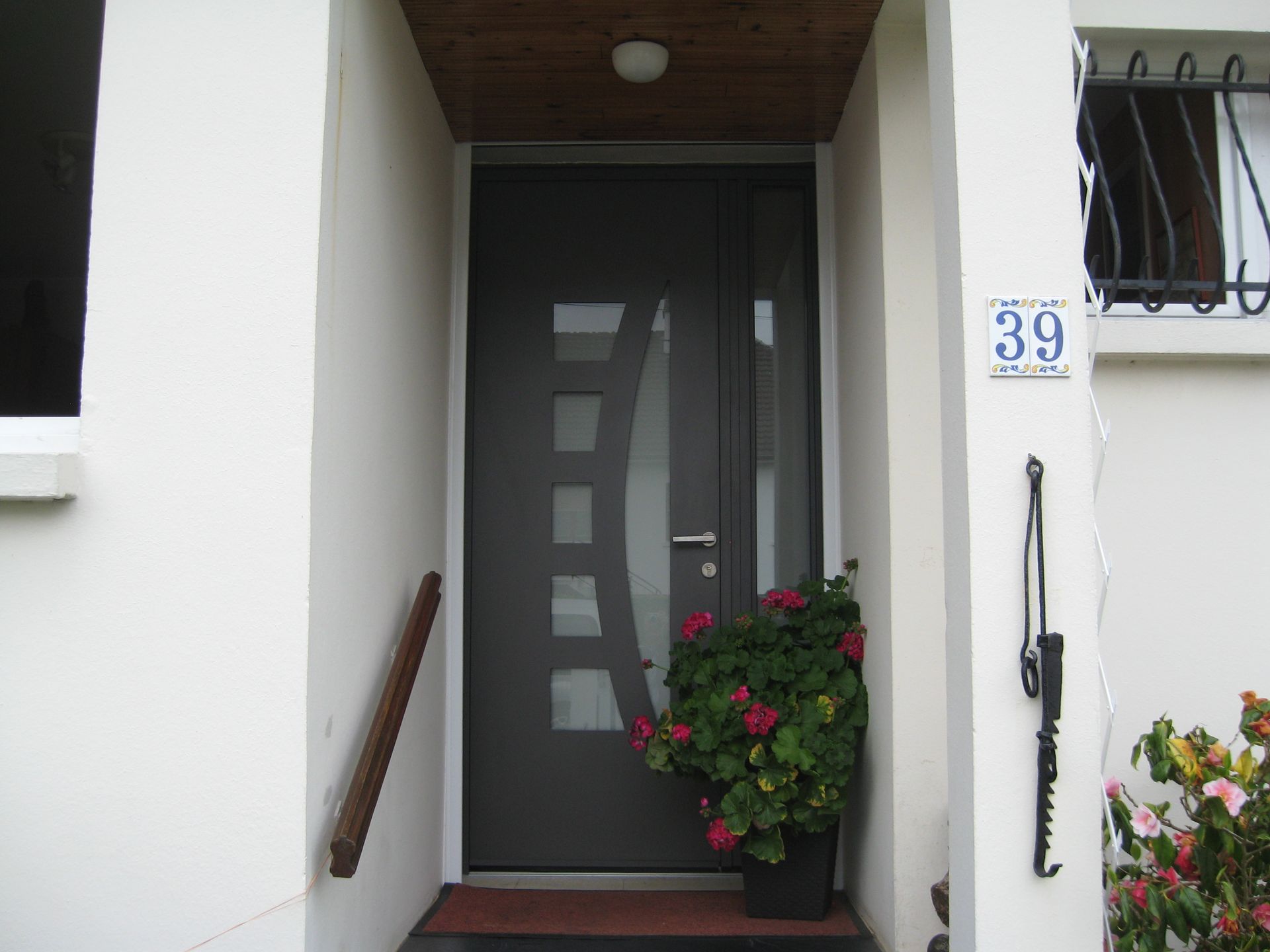 Porte d'entrée grise avec une rampe d'escalier et un pot de fleur à côté.