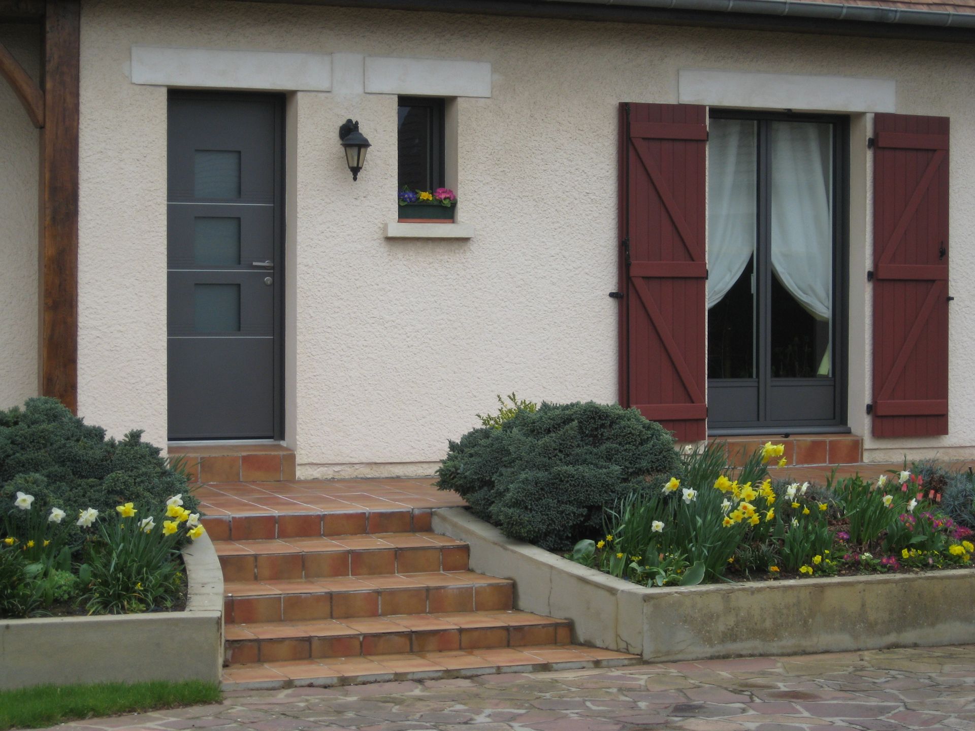 Baie vitrée avec des volets marron près d'une porte d'entrée grise.