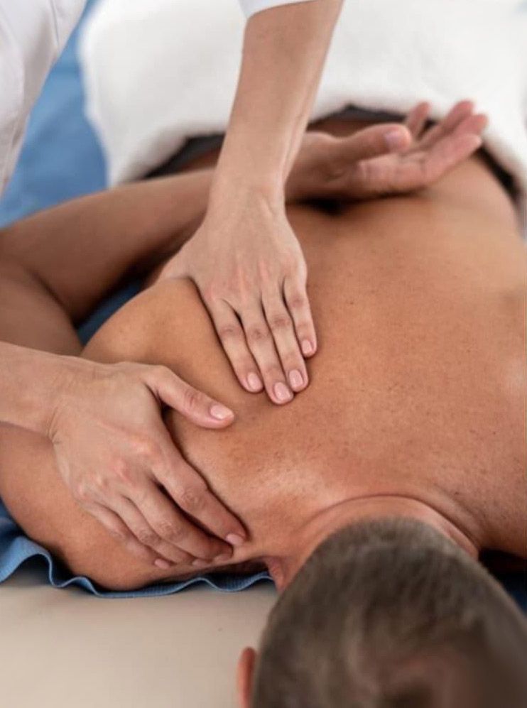 Manos masajeando el hombro de una persona acostada boca abajo en una mesa de masajes.