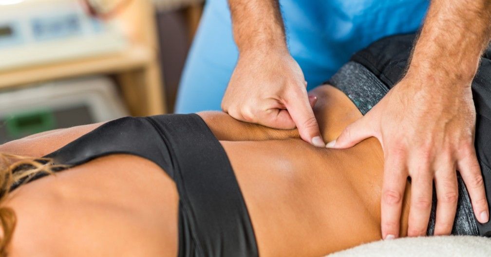 Una persona está arrodillada junto a los pies de otra persona sobre un piso de madera.