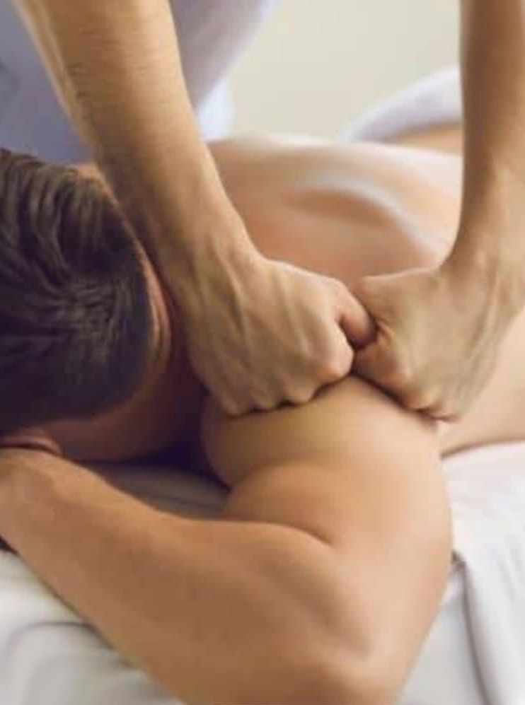 Las manos del masajista masajean el hombro y el brazo de una persona. La persona está tumbada boca abajo en una camilla.