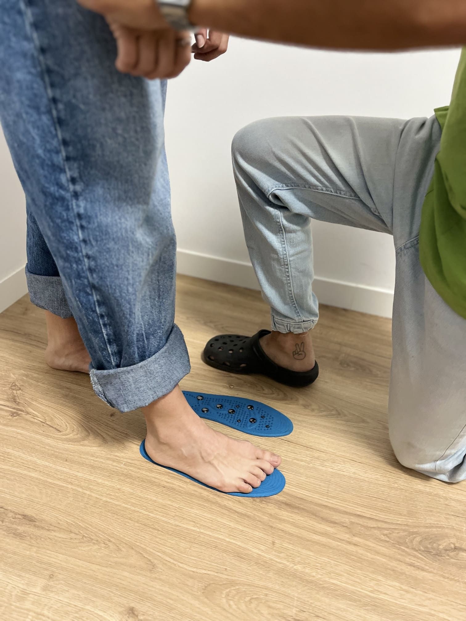 Una persona está arrodillada junto a los pies de otra persona sobre un piso de madera.