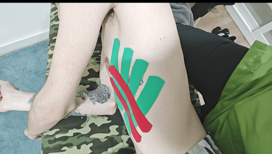 Una persona está colocando cinta verde en la pierna de una persona.