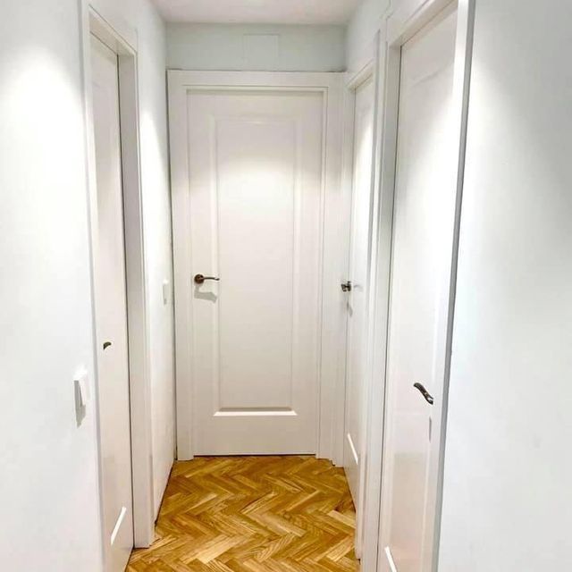 Un pasillo con suelo de madera y puertas blancas.