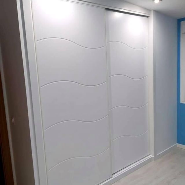Un armario con puertas correderas blancas y una pared azul en un dormitorio.