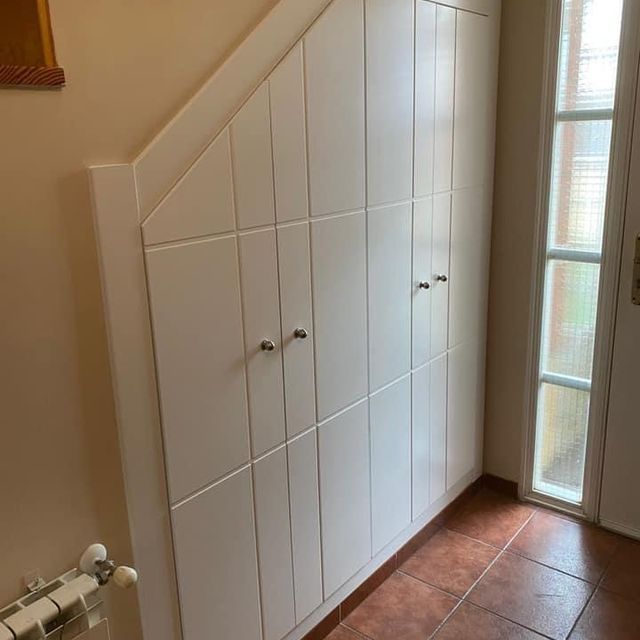 Un pasillo con muchos armarios blancos debajo de una escalera.