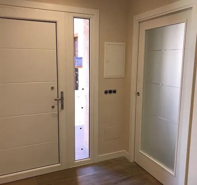 Un pasillo con dos puertas blancas y una puerta de cristal.