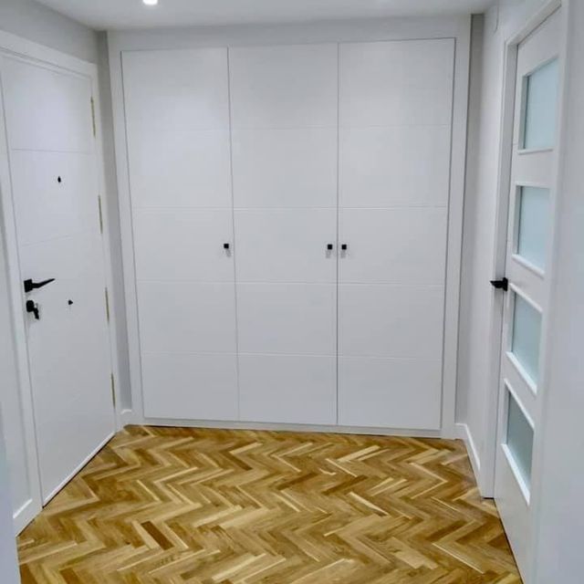 Un pasillo con piso de madera y gabinetes blancos.