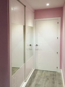 Un pasillo con paredes rosas y una puerta blanca con un espejo en la pared.